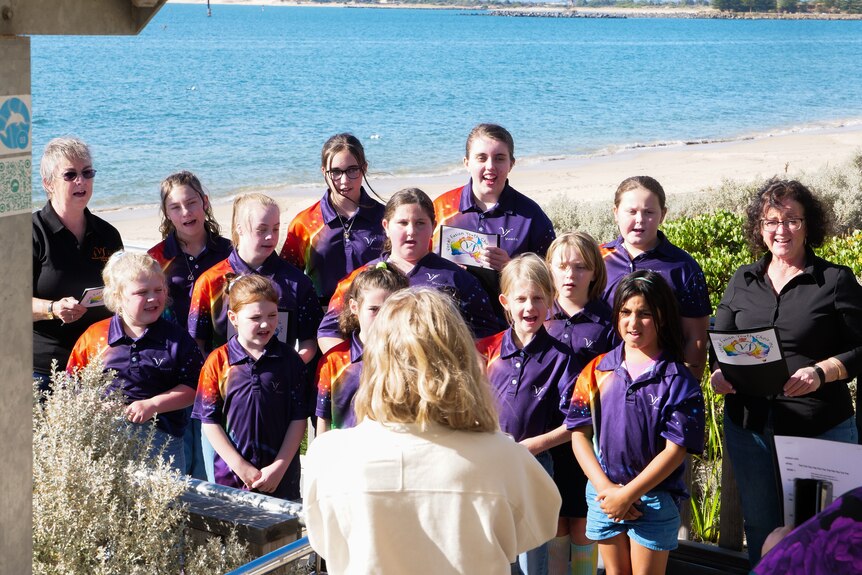 A group of young people singing with two older ladies at a beach. 