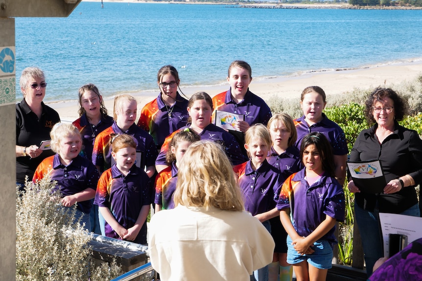 A group of young people singing with two older ladies at a beach. 