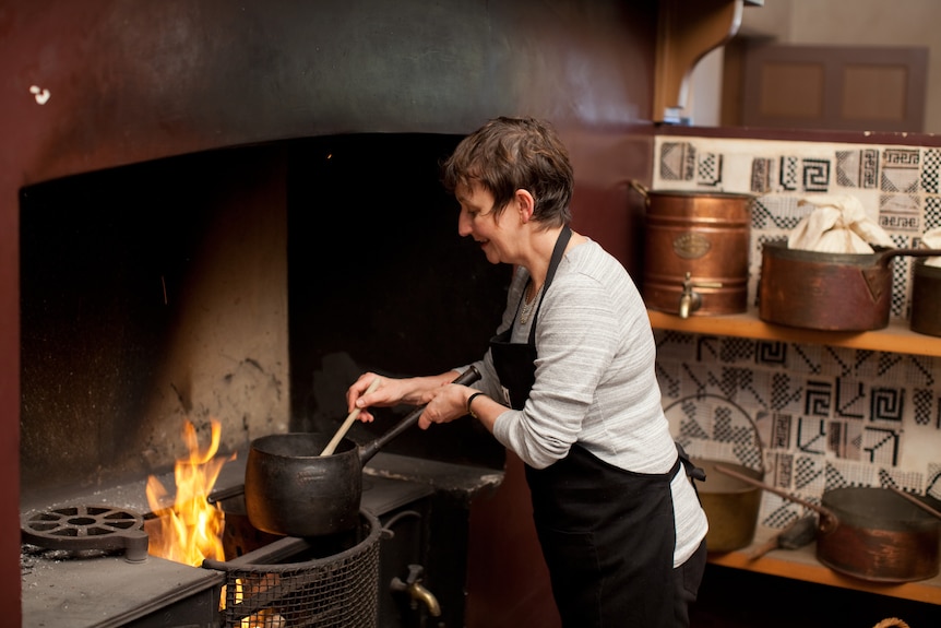 Woman stirring food in an old iron pot over an open flame in the colonial kitchen of Vaucluse House. 