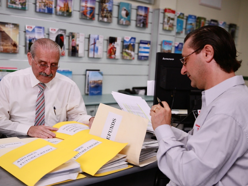 An older man with glasses going through manila folders with another younger man