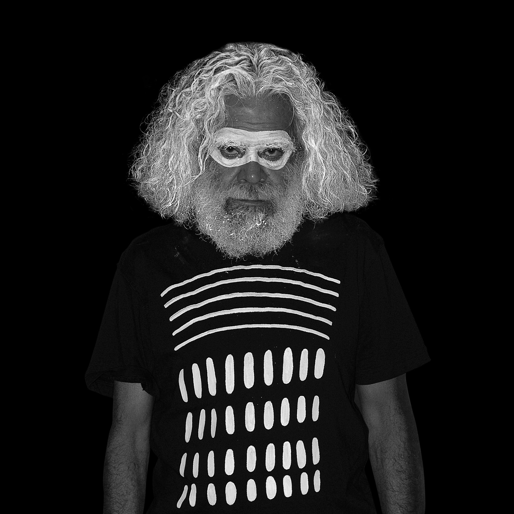 Photograph of Jack Charles, a 70-something Aboriginal man with a white beard, with white ochre smeared across his eyes