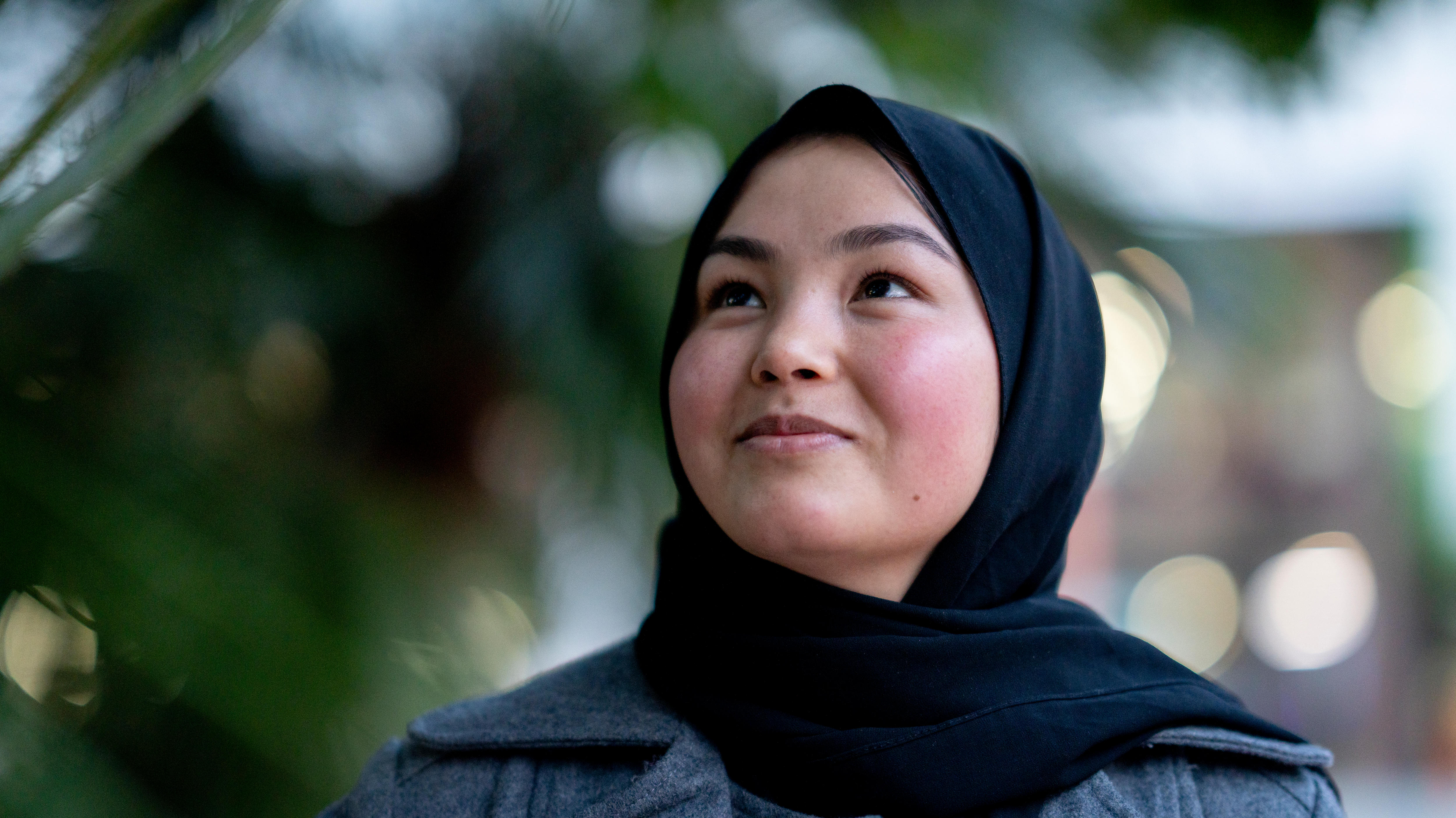 Adiba stands, with a headscarf, looking up towards the sky, pondering