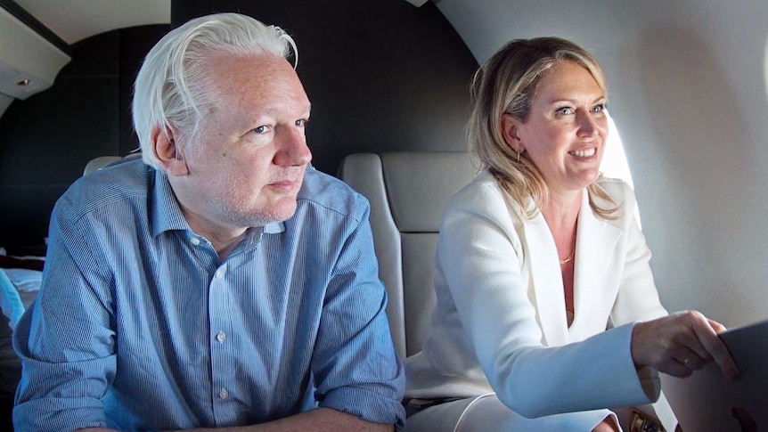 Assange and Robinson sit in plane seats, looking happy.