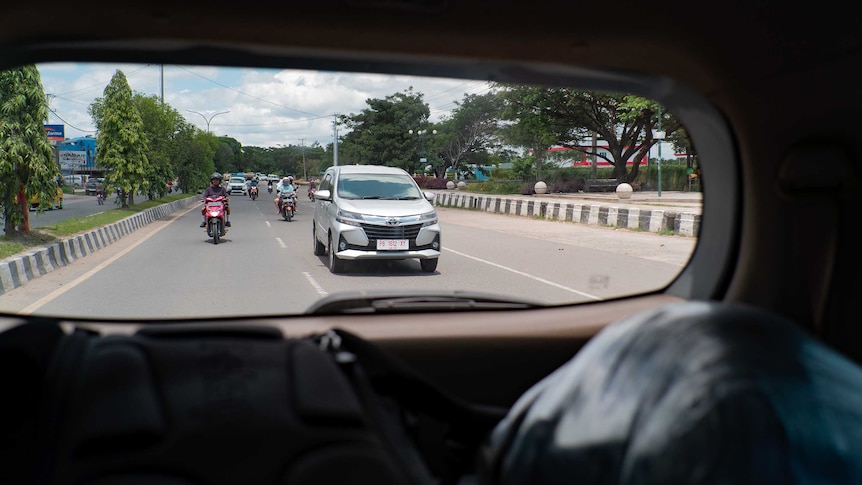 Cars and motorbikes are seen through a car's rear window.