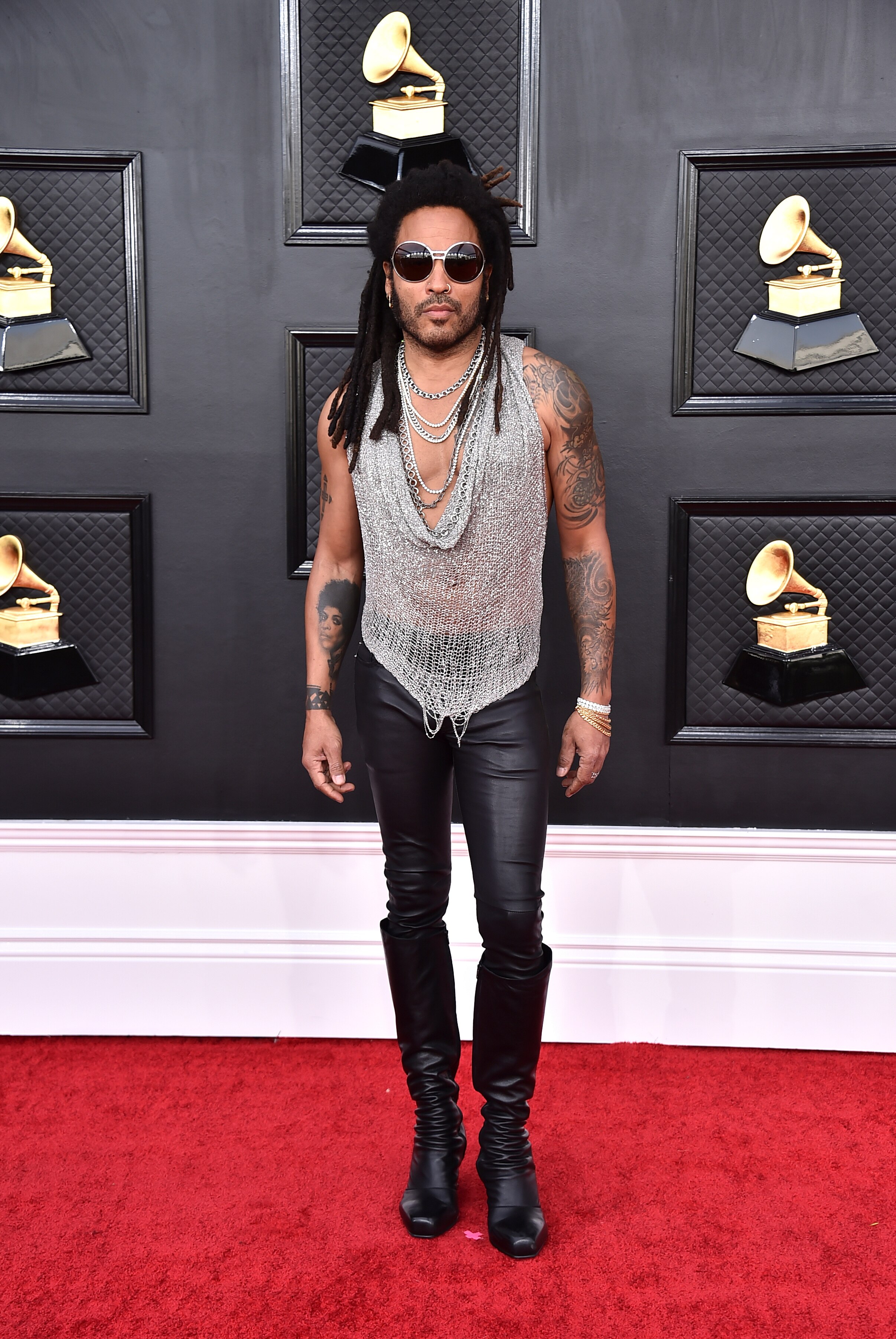lenny kravitz poses on the red carpet wearing a chain mesh silver singlet and tight leather-look black pants with high boots