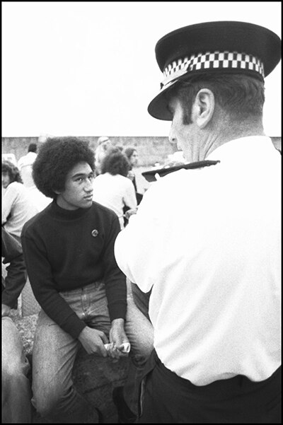 A young Pacific man looks into the eyes of a police officer standing over him. 