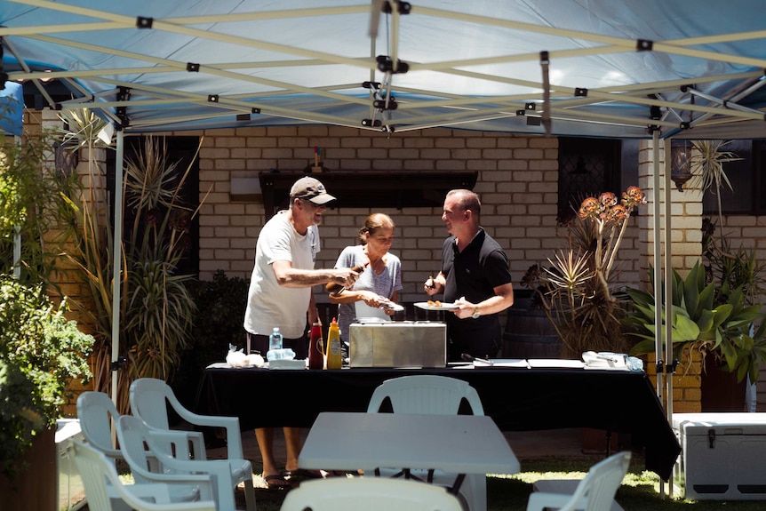 Gary, Karen and Colin stand under a marque dishing up sausages.