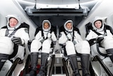 Civilian astronauts wearing white gear and helmets sitting in a space ship ready for take off. 