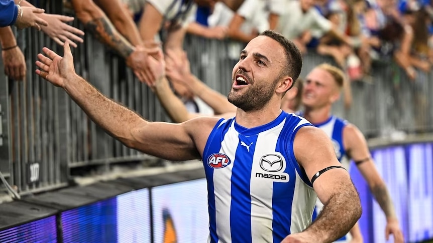 Griffin Logue in his AFL North Melbourne jersey shakes hands with the crowd at a game
