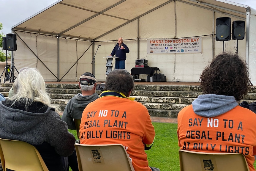 People seated looking at a stage wearing orange shirts that say 'Say No to a Desal Plant at Billy Lights' on the back.