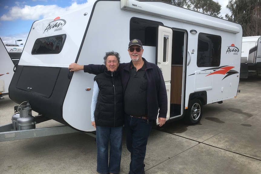A man and a woman smiling in front of a caravan.