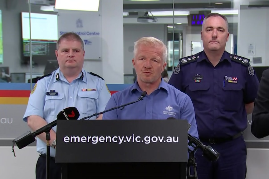 a man in a blue shirt with gray hair stand behind a lectern.