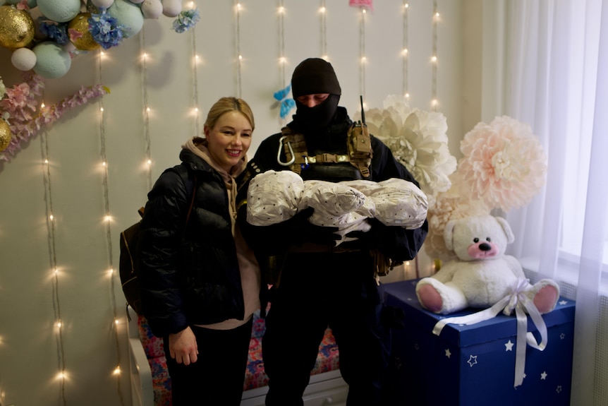 A woman and her husband in SWAT gear in the hospital with their newborn Ivan. 