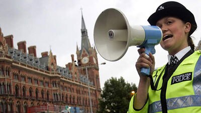 A policewoman uses a megaphone to hold back people from walking towards Kings Cross and St Pancras station after the bomb blasts in London.