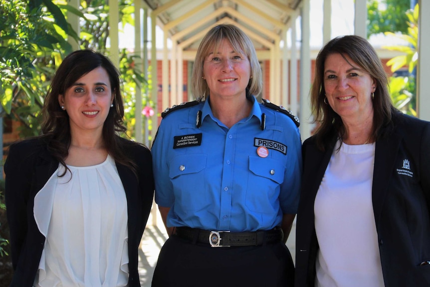 Three women, the central one in a prison officer's uniform, stand side by side.