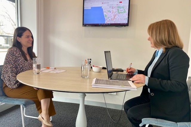 A young first home buyer sits at a table in an office with her mortgage broker 