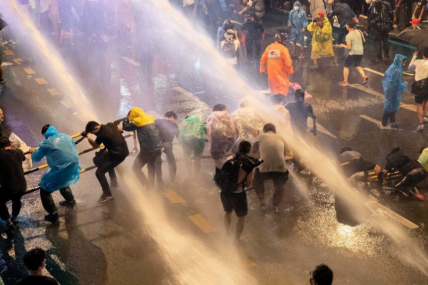 People hunch over in a street as they are sprayed with water