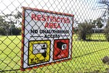 A sign that says "restricted area" is fixed to a chain link fence in front of green grass.