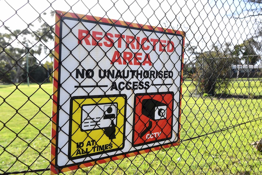 A sign that says "restricted area" is fixed to a chain link fence in front of green grass.