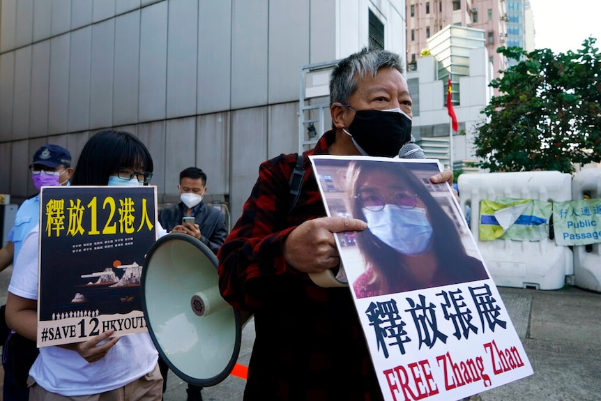 民运人士举着印有中国公民记者张简照片的旧横幅游行。