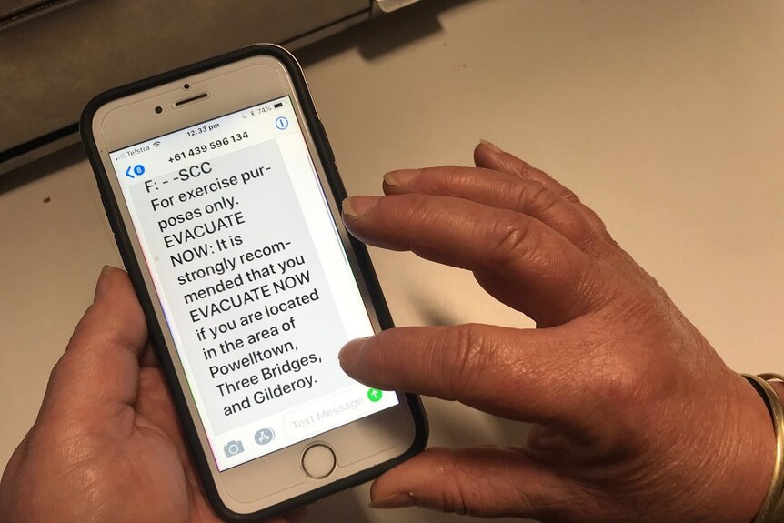 Hands holding a phone, which has a text message saying 'For exercise purposes only. EVACUATE NOW'.