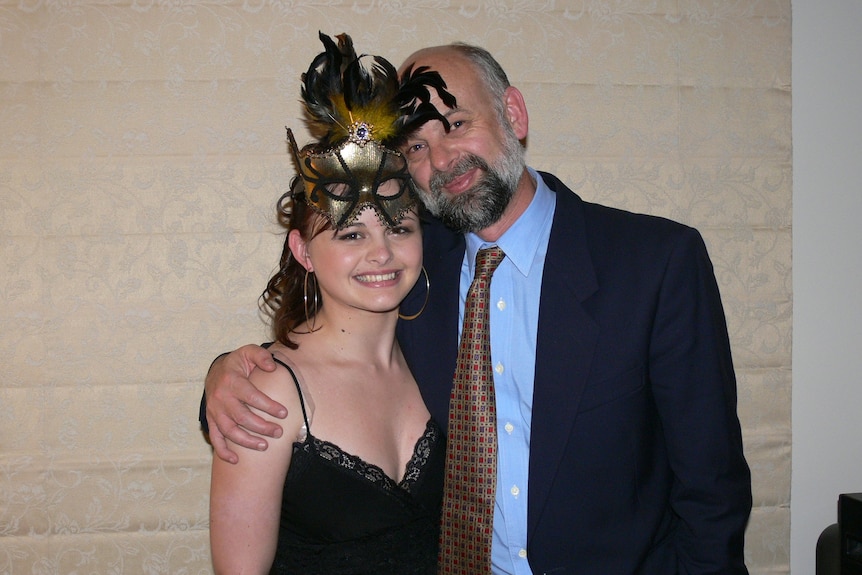 An older man poses with his arm around the shoulders of his younger daughter.