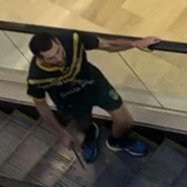 A poor quality photo of a man with a knife on an escalator, taken from above.