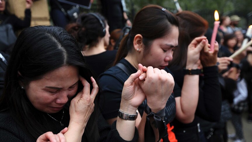 Filipina women hold hands and shed tears during a vigil for victims