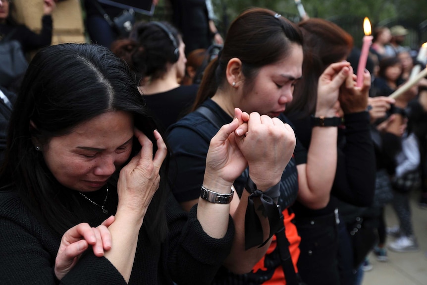 Filipina women hold hands and shed tears during a vigil for victims