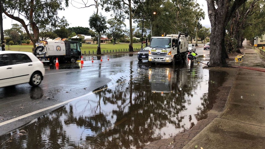 A wide shot of a street in Bayswater with half of the road flooded and a truck pumping water away.
