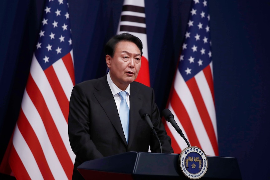 Yoon Suk Yeol stands behind a lectern surrounded by American flags.