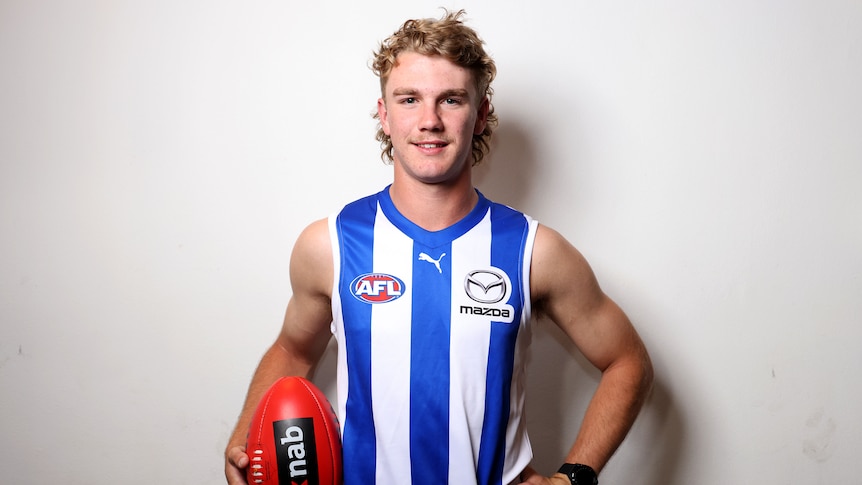An AFL draftee poses for a photograph in a North Melbourne jersey.