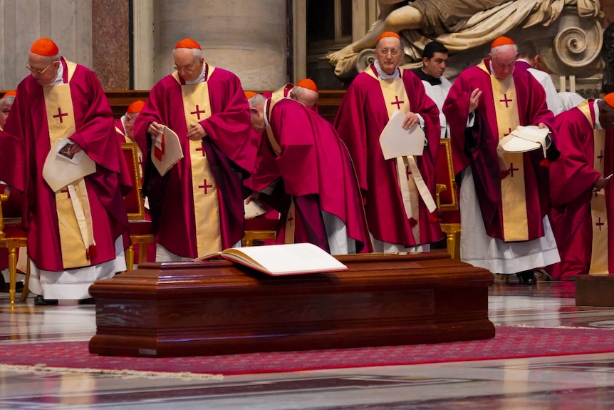 People in religious robes stand around a coffin. 