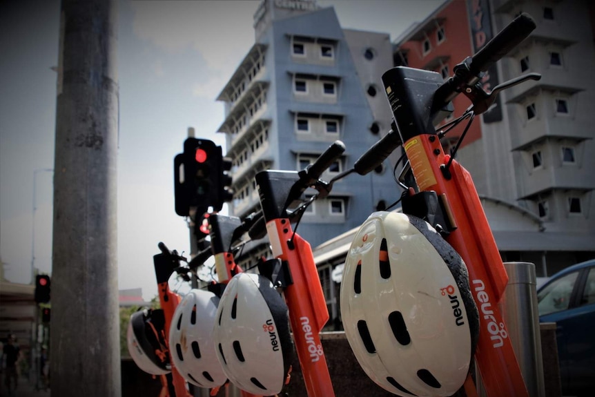 A group of orange e-scooters parked on a sunny day in Darwin city.