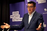 Daniel Andrews at a press conference standing with his arms spread wide.