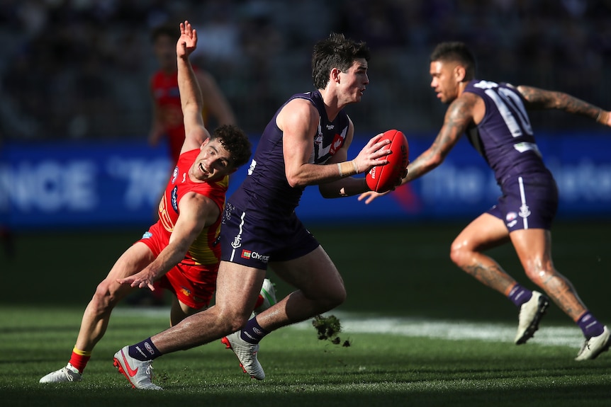 Fremantle's Andrew Brayshaw holds a Sherrin as he runs away from Gold Coast's Sam Flanders during an AFL game.