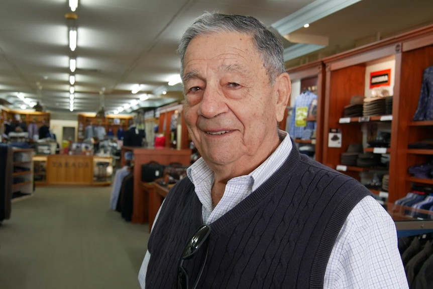 A portrait photo of a man's face, as he stands inside his clothing store, looking out.