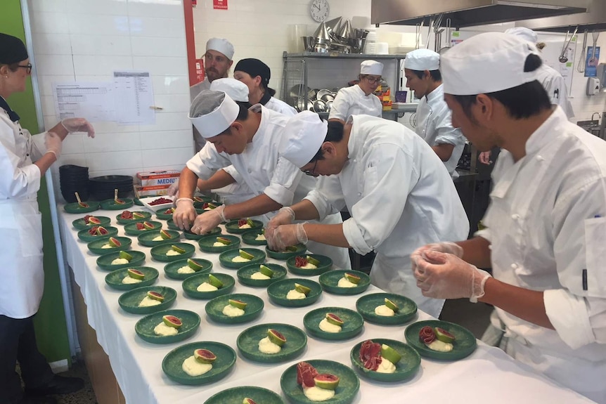 Three students are standing in front of a bunch of bowls and placing food on them