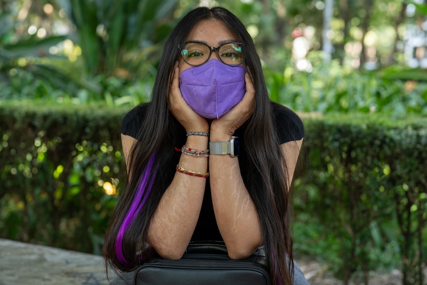 A woman in a purple face mask leans her face in her hands 