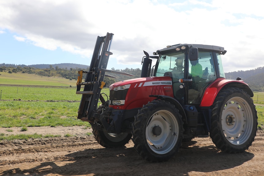 a red tractor with lifting equipment on the front  drives alonmg a dirt road next to a field