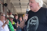 Clive Palmer wearing a Ned Kelly shirt, holds a microphone.