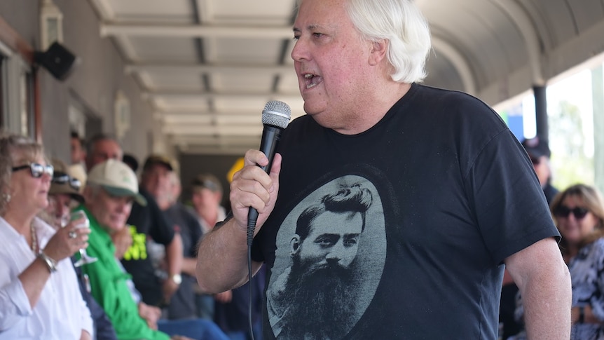 Clive Palmer wearing a Ned Kelly shirt, holds a microphone.