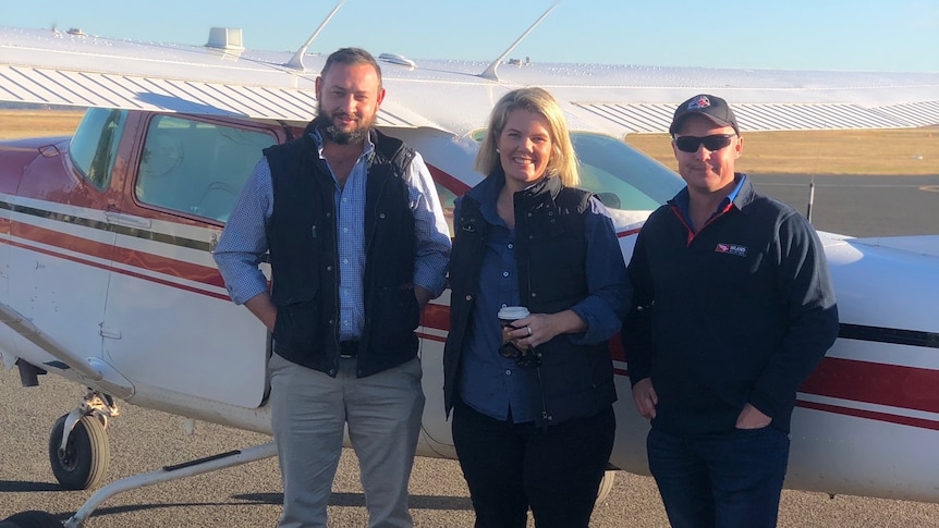 Two male pilots stand in front of a plane with the midwife they are flying to outback NSW