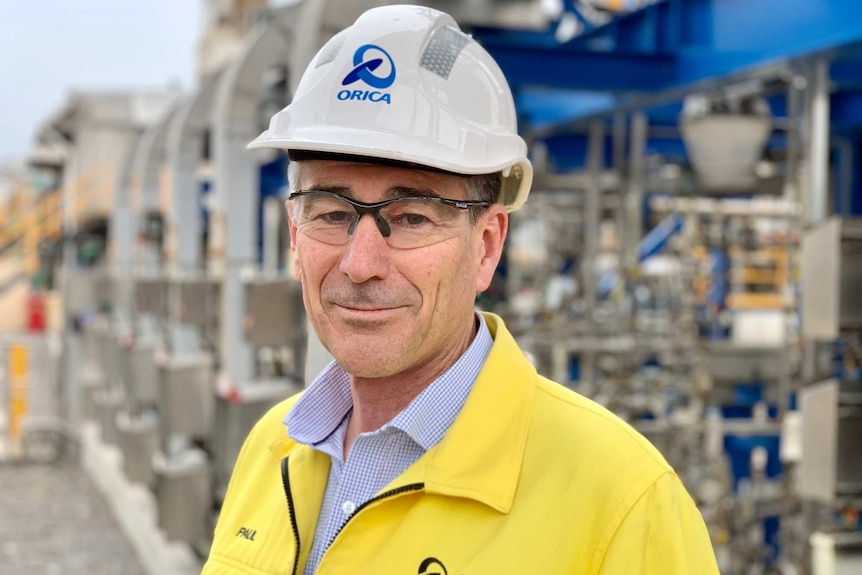 Paul Hastie in a hard hat and high vis vest, factory behind him