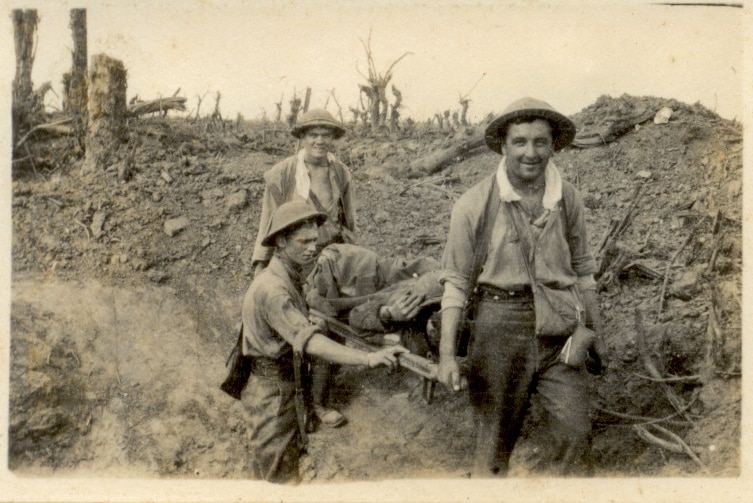 Sepia photo of three soldiers carrying a stretcher with a wounded man through a bombed out field.