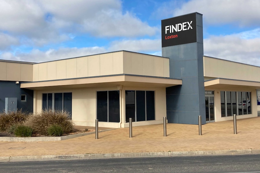 A large one-storey office building with sandy coloured walls and tinted windows. A grey and black sign reads 'Findex Loxton'.
