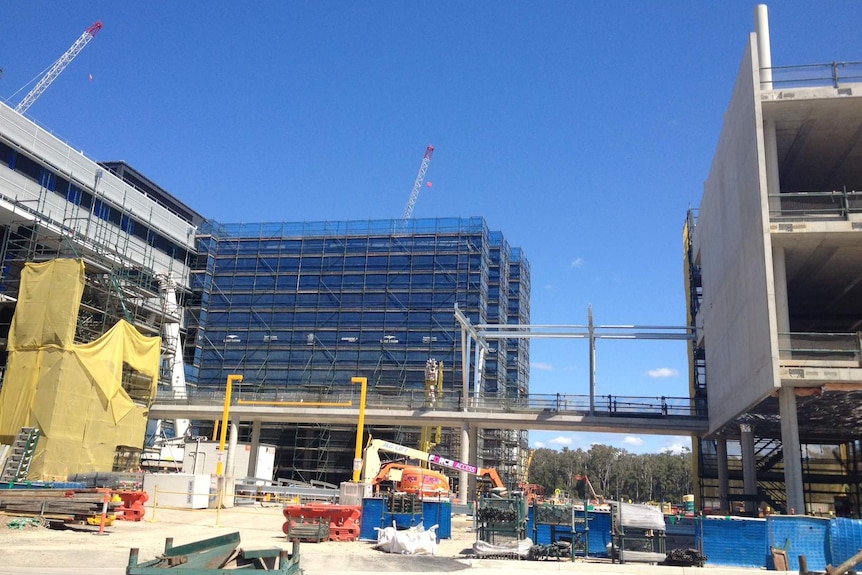 A multi-storey building under construction, with two cranes and heavy scaffolding in place