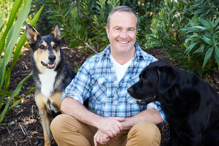 A man sits in a garden with two dogs