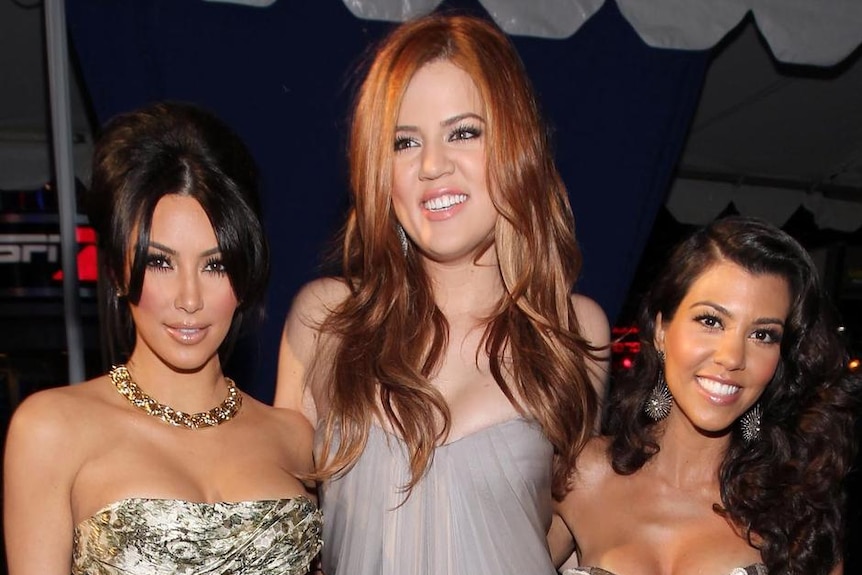Kim Kardashian, Kourtney Kardashian and Khloe Kardashian stand together smiling.