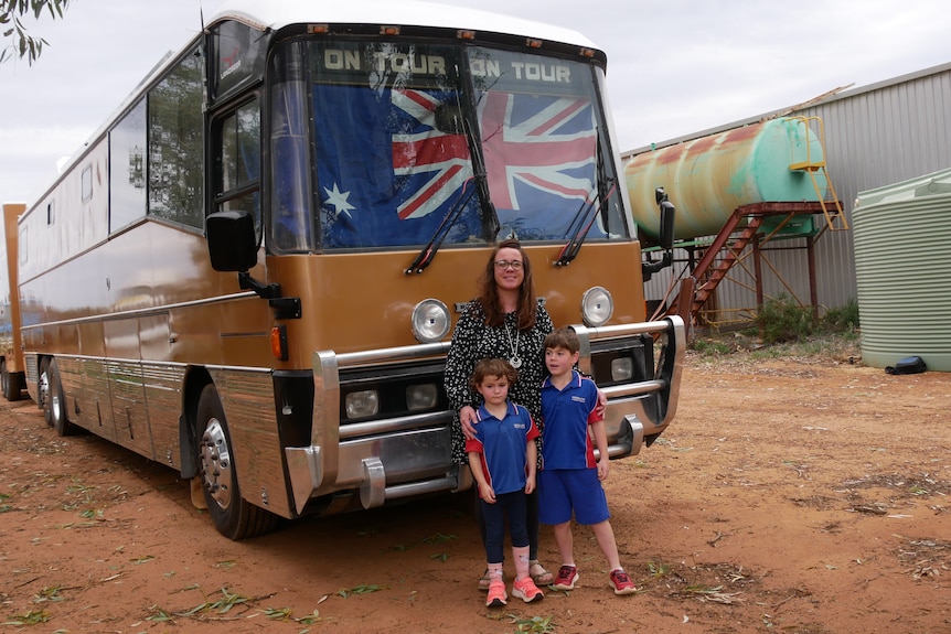 A mum and two children stand in front of a bus with an Australian flag in the window.